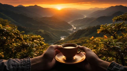 Foto op Canvas Hand holding a cup of hot tea and natural view of mountain landscape at sunset © MBRAMO