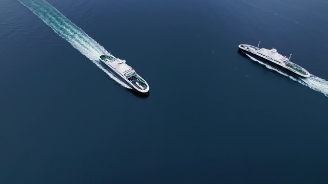 Aerial drone shot of two passenger and vehicle ferries cross each other path in open water at sea. Maritime ferry route in between islands