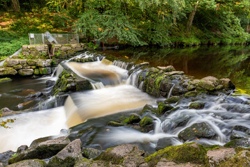 Long exposure of the river Teign flowing through Castle Drogo weir in Dartmoor - obrazy, fototapety, plakaty