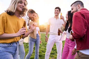Group of friends drinking beer having fun in a party at the park. having fun in this celebration. They dance and laugh while the sunset over the grass. They enjoy holidays.