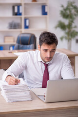 Fototapeta premium Young male employee and too much work at workplace