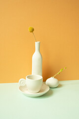Minimal white ceramic coffee cup and vase of flower on mint green table. orange wall background