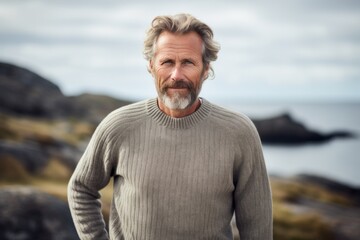 Portrait photography of a Swedish man in his 50s wearing a cozy sweater against a beach background