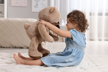Cute little girl with teddy bear on floor at home