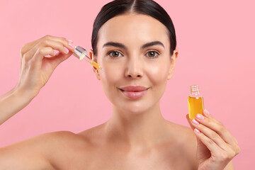 Fototapeta premium Beautiful young woman applying serum onto her face on pink background
