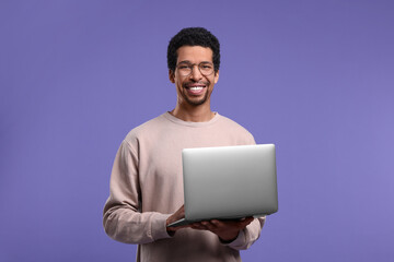 Smiling man with laptop on purple background