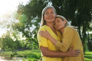 Naklejka premium Family portrait of happy mother and daughter hugging in park on sunny day. Space for text