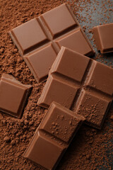 Delicious milk chocolate and cocoa powder on grey table, closeup