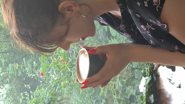 Close up of young woman drinks coffee latte. Mobile video format 