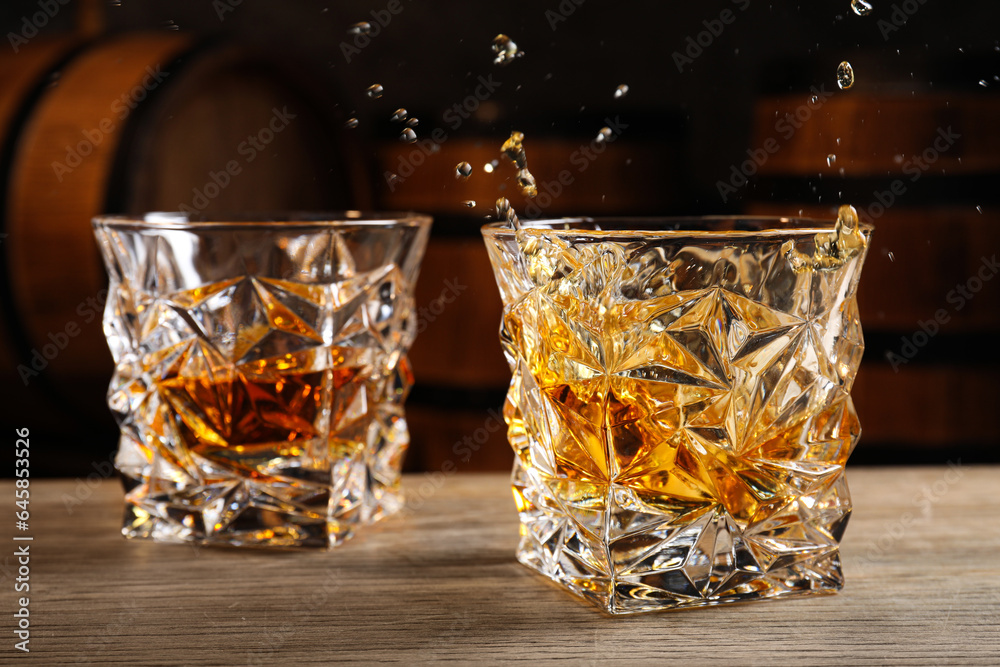 Sticker Glasses with whiskey on table against wooden barrels, closeup