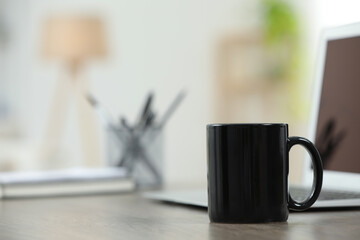 Black ceramic mug and laptop on wooden table indoors