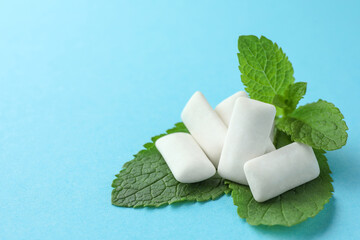 Tasty white chewing gums and mint leaves on light blue background, closeup. Space for text