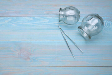 Glass cups and tweezers on light blue wooden table, flat lay with space for text. Cupping therapy