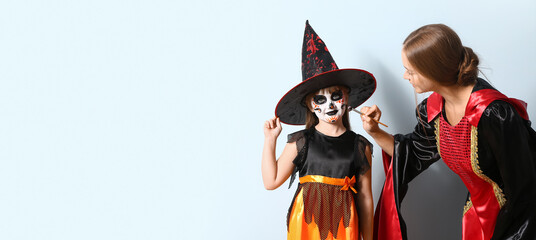 Mother and her little daughter in costumes preparing for Halloween party on light background with space for text