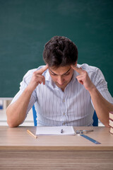 Young male teacher in front of green board