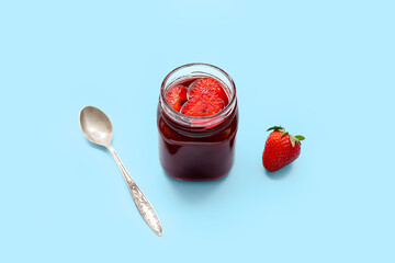 Jar of sweet strawberry jam on blue background