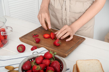 Woman cutting fresh berries for preparing sweet strawberry jam at table in kitchen