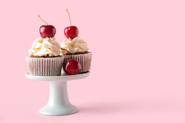 Stand with tasty cherry cupcakes on pink background