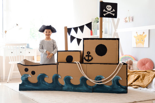 Cute little pirate playing in cardboard ship at home