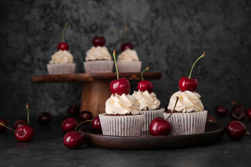 Plate with tasty cherry cupcakes on black background