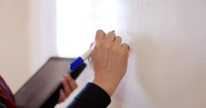 Whiteboard, tablet and teacher hands writing in a classroom with information from tablet for education. Marker, notes and closeup of person in university or college presentation to share knowledge