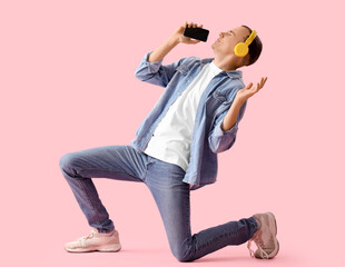 Young man in headphones with mobile phone singing on pink background
