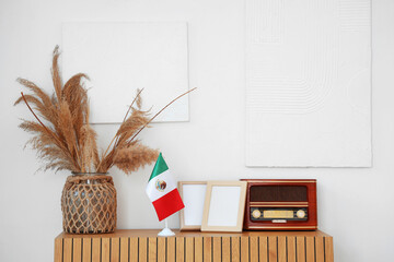 Mexican flag with blank frames, vase and retro radio receiver on commode in room