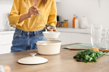 Young woman pouring chicken soup into bowl in kitchen, closeup