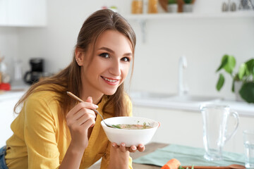 Young woman with bowl of chicken soup in kitchen, closeup