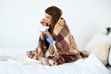 Ill young woman eating chicken soup in bedroom