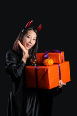 Young Asian woman dressed for Halloween with gifts on black background