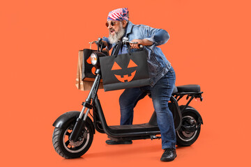 Mature biker with Halloween gift bags and scooter on color background