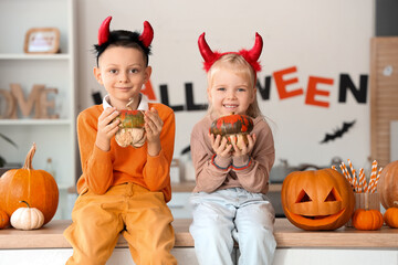 Little children with devil horns and Halloween pumpkins in kitchen