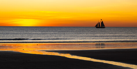 Schooner sailboat passing Broome during stunning sunset, Western Australia