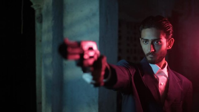 Professional gun-man with long hair in a blue colored suit in a neon light setting pointing gun at someone offscreen. Cinema like HD stock footage.