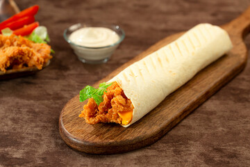 hand holding Tortilla wraps with crispy chicken breast, lettuce and vegetables, served with garlic cream sauce