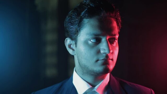 Cinema-like footage under neo-noir lighting of a business in a blue-colored suit and white shirt standing and looking for someone in the crowd. HD high-quality stock footage.
