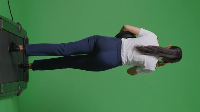 Back View Full Body Of Asian Woman Pilot Talking On Smartphone While Walking On Treadmill In The Green Screen Background Studio
