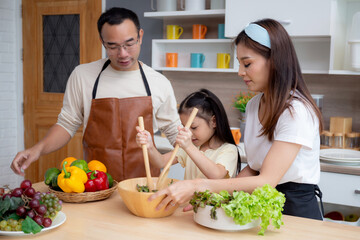 Happiness asian family with father, mother and daughter preparing cooking salad vegetable food together in kitchen at home, happy dad, mom and kid cooking breakfast with salad, lifestyles concept.