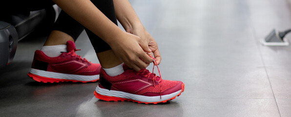 Closeup young woman tying shoelace with hands for jogging in fitness gym sport club, female preparing workout and exercise with wearing sportswear and sneaker, healthcare and motivation.