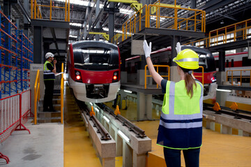 Young caucasian engineer woman or worker signal while engineer man checking electric train for planning maintenance in station, transport and infrastructure, inspector check service transport.