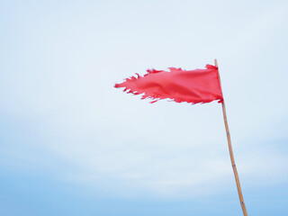 Tearing red flag waving against blue sky background. - 645882115