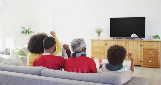 Biracial family watching tv with rugby ball at stadium on screen