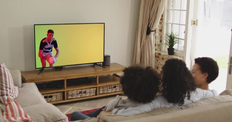 Biracial family watching tv with caucasian male rugby player jumping with ball on screen - Powered by Adobe