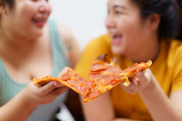 Happy oversize fat Asian women enjoy eating a pizza, hamburger, and French fry with drinking cola soda together. Unhealthy eating and unhealthy lifestyles concept.