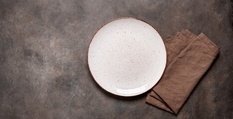 White plate with a brown napkin on a brown rustic background. Top view, flat lay, copy space. Banner.