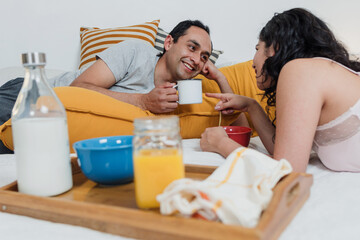 Obraz na płótnie Canvas Latin couple having breakfast in bed at home in Mexico Latin America, hispanic people having fun