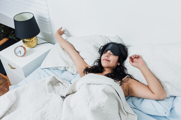 latin woman using sleeping mask and waking up in bed in the morning at home in Mexico Latin...