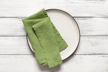 White plate with green napkin on a white wooden table. Top view, flat lay, copy space.
