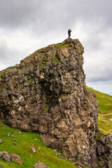Fototapeta premium Hiker climbs on top of a rock formation taking a photo on the Isle of Skye, Scotland.